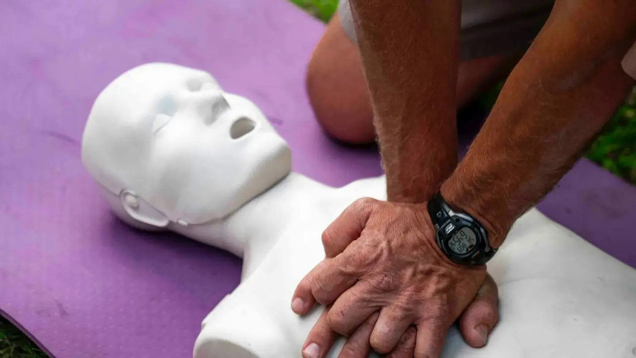 Mãos posicionadas sobre o tórax de um manequim de treinamento durante prática de reanimação cardiopulmonar.