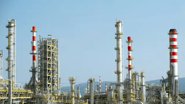 Torres e tubulações de uma refinaria de petróleo com faixas vermelhas e brancas, instalação classe III da NR-20.