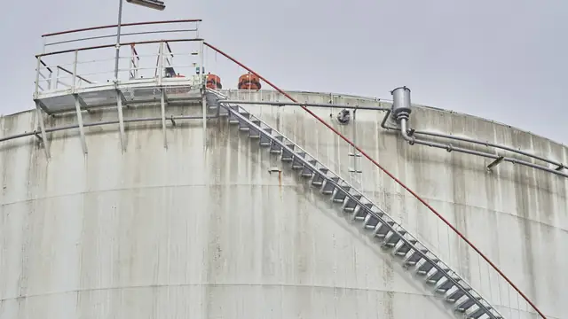 Tanque industrial de aço com escada de acesso e guarda-corpo, ambiente típico de entrada em espaço confinado.