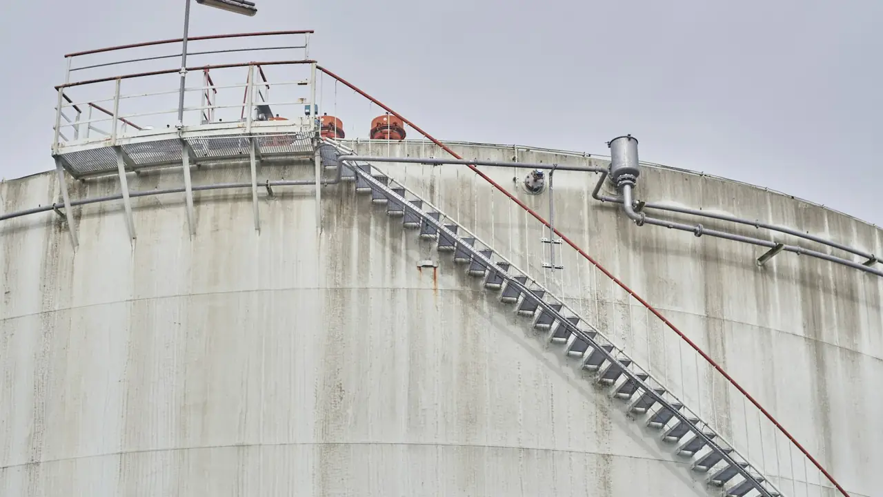 Tanque industrial de aço com escada de acesso e guarda-corpo, ambiente típico de entrada em espaço confinado.