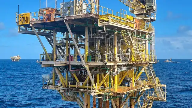 Plataforma de petróleo offshore com guindaste e estrutura amarela sobre o mar.