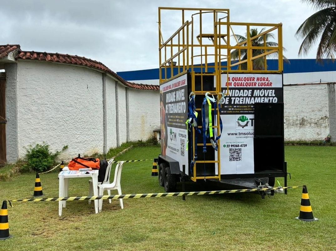 Vista traseira do módulo de treinamento, com escada de acesso vertical enjaulada e plataforma superior utilizadas nas práticas de espaço confinado e altura.